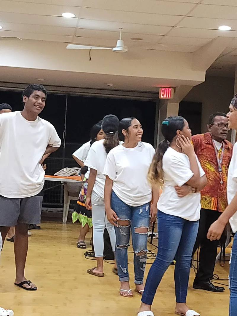Youth group members in white t-shirts smiling and gathered together at a church event.